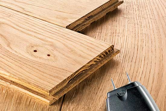 Deux petits trous dans une lame de parquet en chêne, à côté d'un humidimètre à broches.